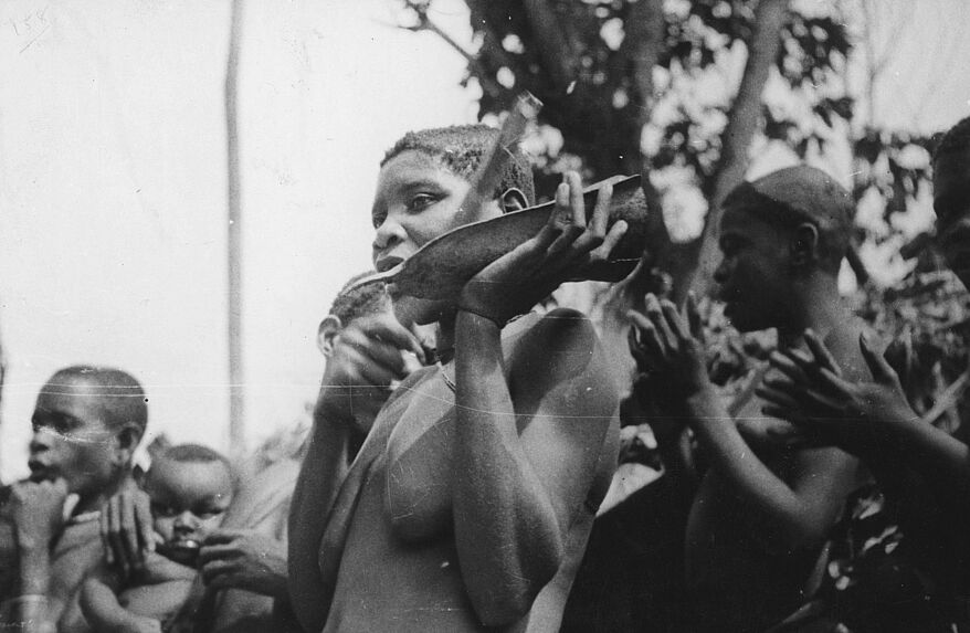 Femme Babinga frappant une cloche de fer