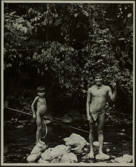 Sans titre [un jeune homme et un petit garçon de face, en pied, tiennent deux longues tiges en bois pour la pêche ? Le petit garçon tient également un arc. Ils sont debout sur des pierres de la rivière]
