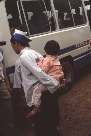 Neitian [femme portant un enfant sur son dos avec les bras, près d'un minibus]