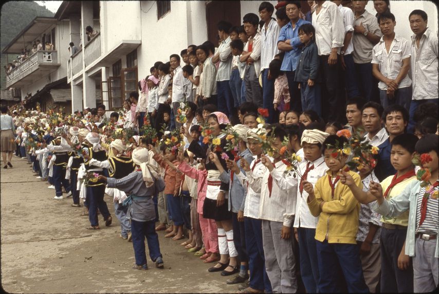 Début réception Bibei [enfants alignés en costume dans la rue tenant des fleurs à la main]
