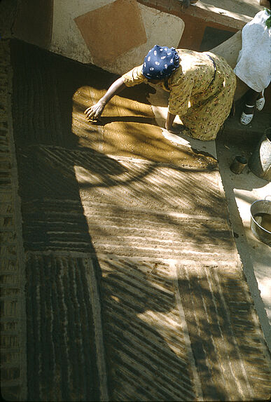 Sans titre [femme venda réalisant des motifs en terre sur le sol d'une construction]