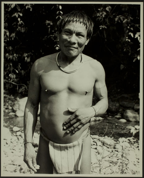 Sans titre [homme debout, en pagne, avec un collier et des bracelets au bord d'une rivière]